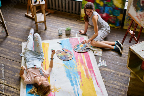 Carefree female artists resting in art studio creating paintings on canvas during hobby pastime, happy Caucasian women dressed in casual clothes communicate and discuss technique of painting