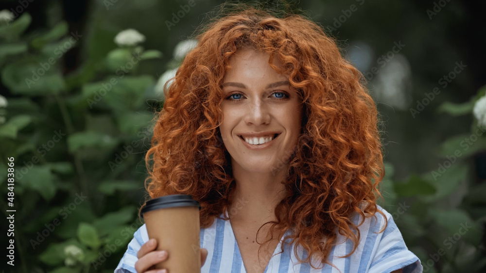 Naklejka premium cheerful redhead woman holding paper cup outdoors.