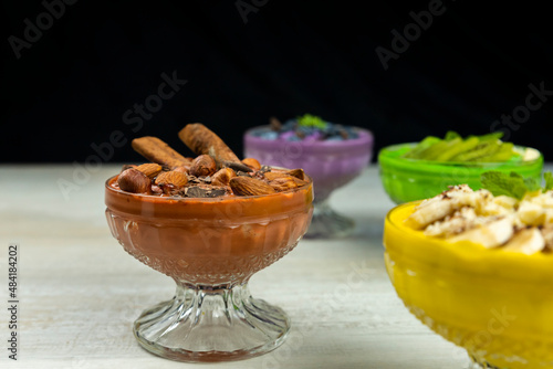 Smoothie or pudding with chocolate, hazelnuts and almonds served in a bowl for breakfast with several other smoothies in background photo
