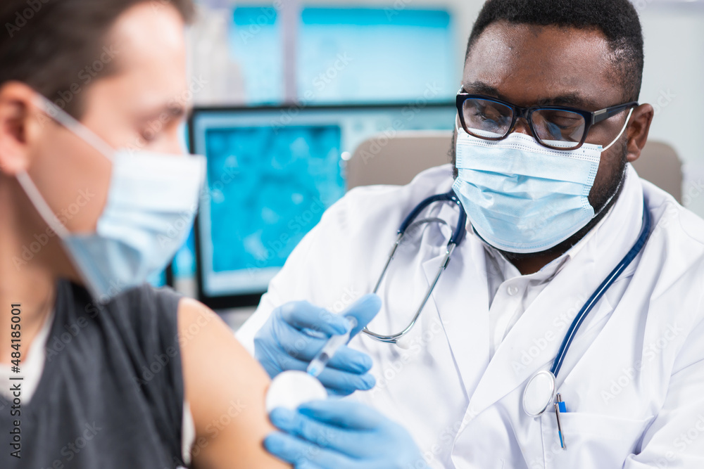 African-American doctor makes a coronavirus vaccine using a syringe and hypodermic needle. Professional medical worker and patient at the hospital office. Vaccination and safety. African-American doctor makes a coronavirus vaccine using a syringe and hypodermic needle. Professional medical worker and patient at the hospital office. Vaccination and safety.
