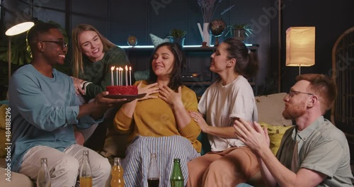 Happy beautiful young Hispanic woman blows on birthday cake with diverse friends at fun confetti celebration house party photo