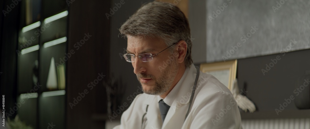Fototapeta premium Portrait of Caucasian doctor delivering telemedicine consultation to a patient from his office. Telehealth, telemedicine, remote consultation service. Coronavirus, COVID-19