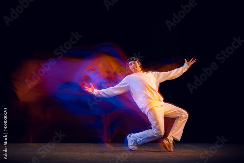 Fototapeta Naklejka Na Ścianę i Meble -  Dynamic portrait of male hip-hop dancer dancing isolated on dark background in mixed neon light. Youth culture, hip-hop, movement, style and fashion, action.