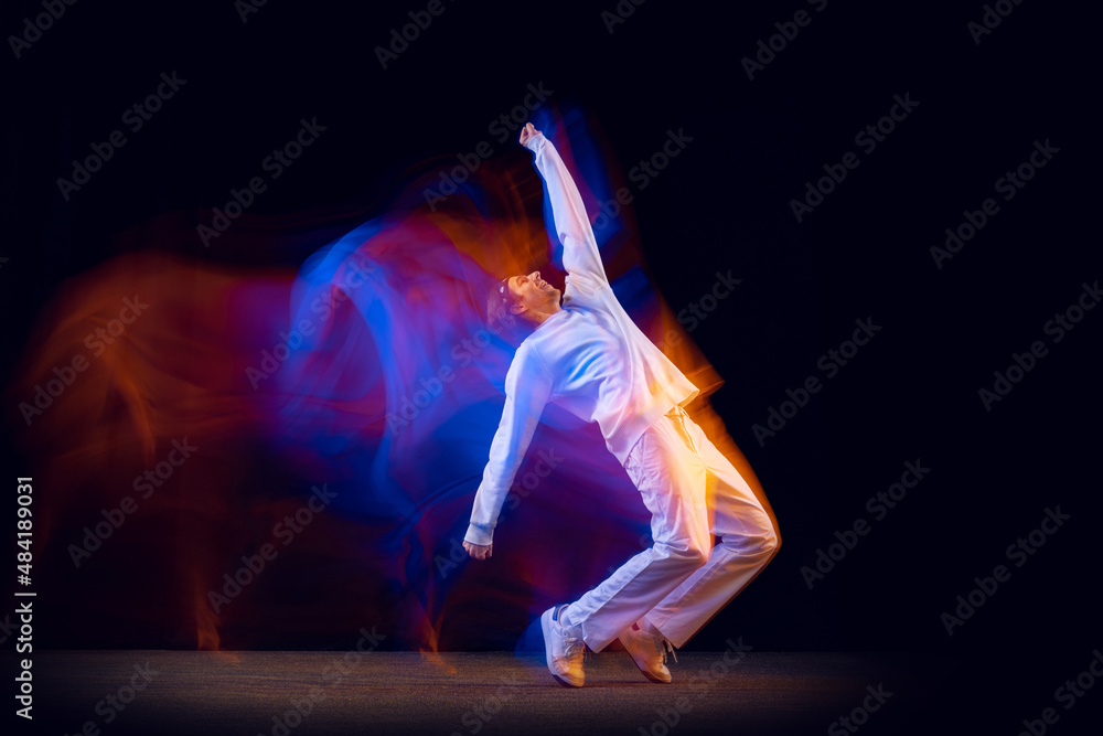 Sportive, emotional man, dancer dancing hip-hop isolated on dark background in mixed neon light. Youth culture, hip-hop, movement, style and fashion, action.