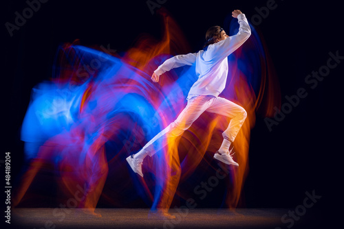 Flexible man in sports white suit dancing hip-hop isolated on dark background in mixed neon light. Youth culture, hip-hop, movement, style and fashion, action.