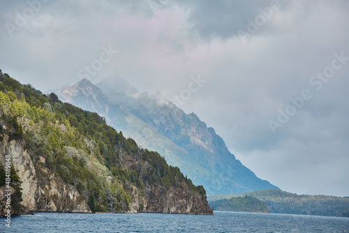Lake in Argentinian Patagonia with turquoise water and trees in the background between mountains. Cloudy day with clouds between the mountains.