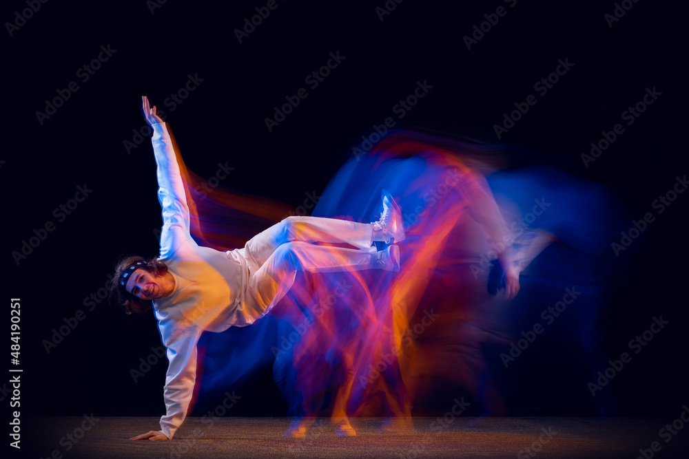 Stylish man in sports white suit dancing hip-hop isolated on dark background in mixed neon light. Youth culture, hip-hop, movement, style and fashion, action.