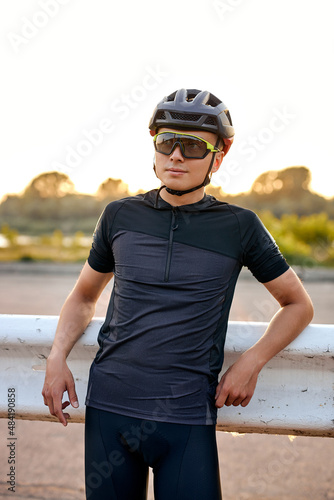 Biker male resting during riding the bike in countryside. Young caucasian athlete in cycling gear practising outside on nature background. Travel and extreme sport concept. at sunset summer season © alfa27