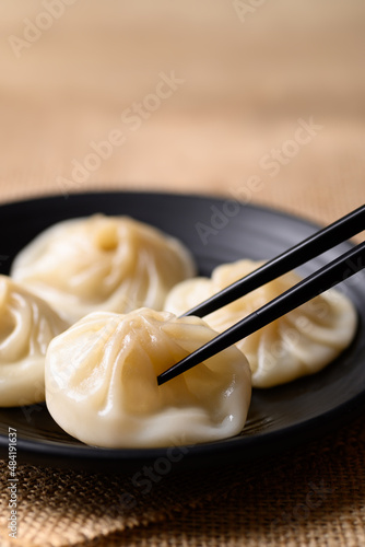 Xiao long bao, small Chinese steamed bun filling with minced pork on black plate eating by use chopsticks