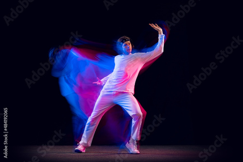 Fototapeta Naklejka Na Ścianę i Meble -  Youth dances. Dynamic portrait of hip-hop dancer in action, motion isolated on dark background in mixed neon light. Youth culture, hip-hop, style and fashion