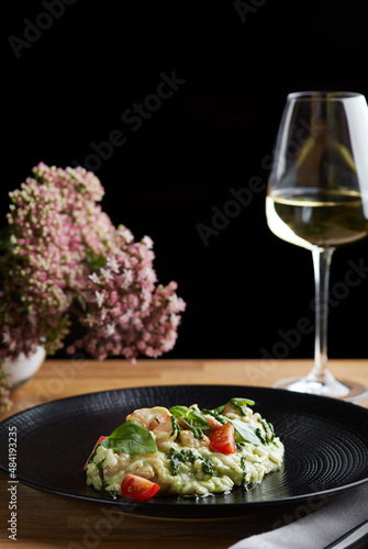 risotto with pesto  basil and cherry tomatoes closeup in black plate on wooden table. risotto on wooden table restaurant with glass of wine