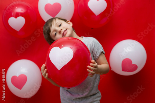 The boy with heart balloons congratulates with valentine's day, on a red background.