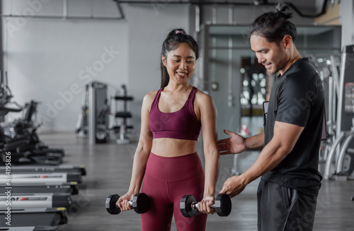 Asian woman exercises with personal trainer in gym. Asian healthy woman doing arms workout in fitnees with personal coach.