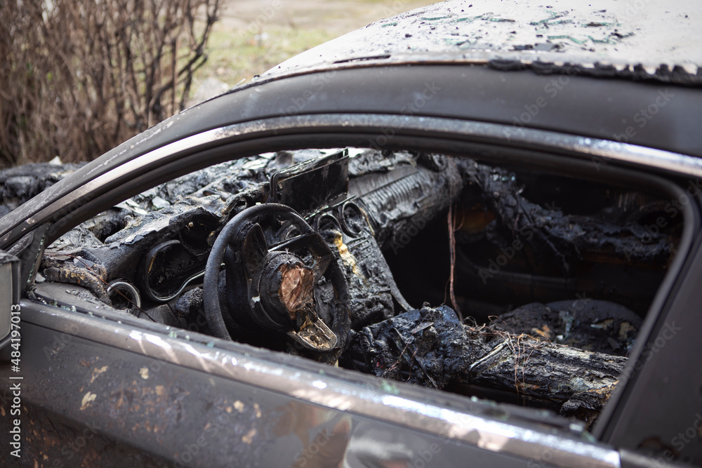 Burnt car interior close-up. Steering wheel and dashboard. Car after the fire. Car wreck burned by vandals or after explosion. Car accident on the road due to speeding.