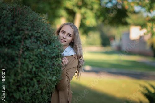 Portrait of a young beautiful fair-haired girl in a beige raincoat in a summer park.