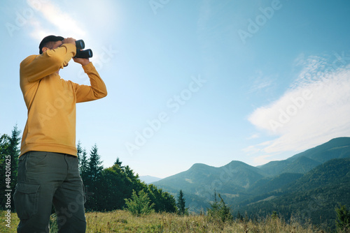 Man with binoculars in mountains on sunny day, low angle view. Space for text