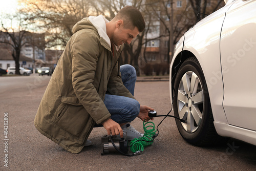 Quadro em tela Handsome man inflating car tire with air compressor on street
