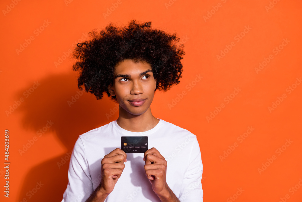 Photo of handsome doubtful guy dressed white shirt showing credit card empty space isolated orange color background Photo of handsome doubtful guy dressed white shirt showing credit card empty space isolated orange color background