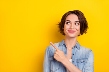Photo of young lovely woman look indicate finger empty space promo ads banner isolated over yellow color background