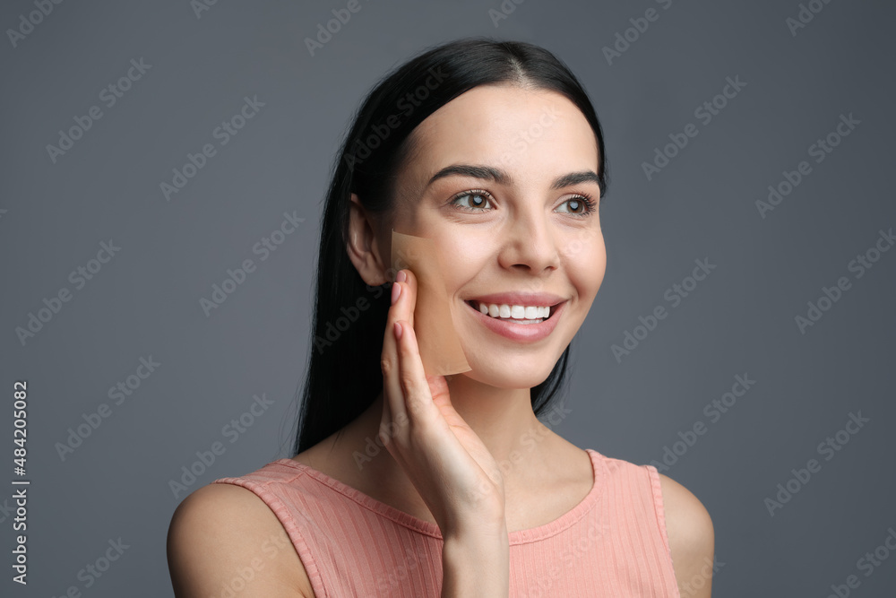 Beautiful woman using mattifying wipe on grey background Beautiful woman using mattifying wipe on grey background
