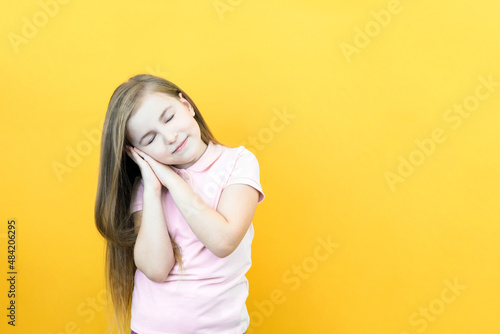 cute smiling sleepy calm girl with closed eyes folded her palms under her head. dreaming on yellow background