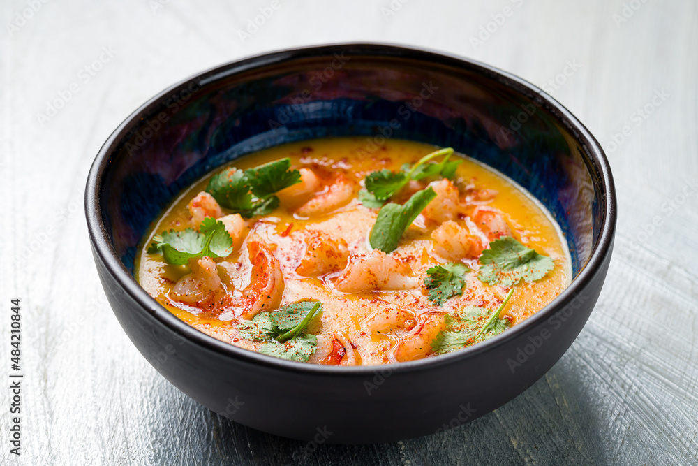 Tom Yam soup with shrimps on blue bowl on grey table