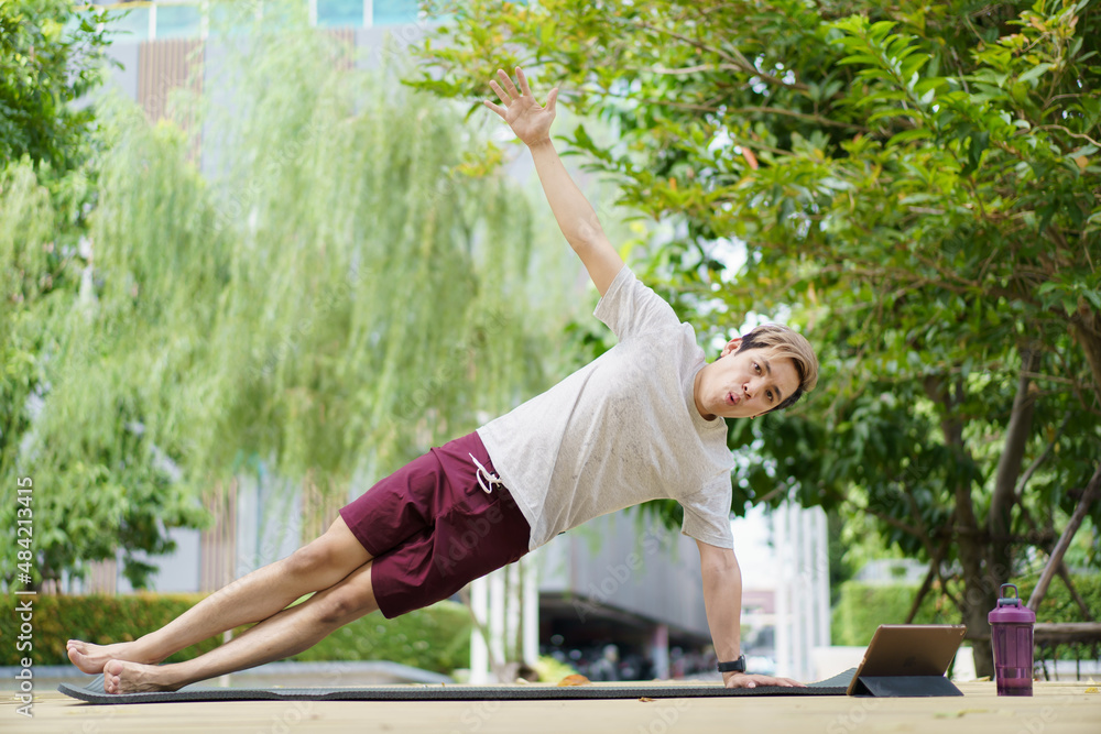 Fototapeta premium Active sportsman doing a side plank exercise and making a video call with a friend.