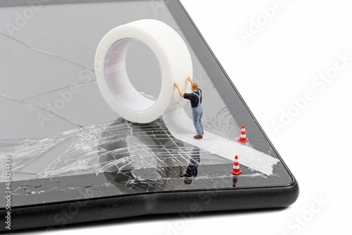 A miniature workman repairing a broken mobile phone tablet touchscreen with a roll of sticky tape