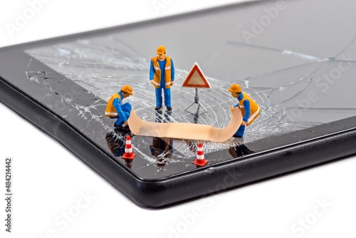 A team of miniature workmen repairing a broken mobile phone tablet touchscreen with a first aid plaster