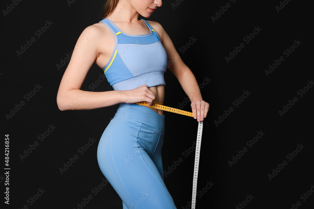 Woman in sportswear measuring waist with tape on black background, closeup. Space for text Woman in sportswear measuring waist with tape on black background, closeup. Space for text