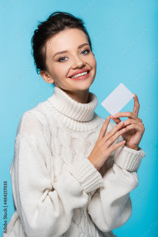 Cheerful woman in white knitted sweater holding blank card isolated on blue. Cheerful woman in white knitted sweater holding blank card isolated on blue.
