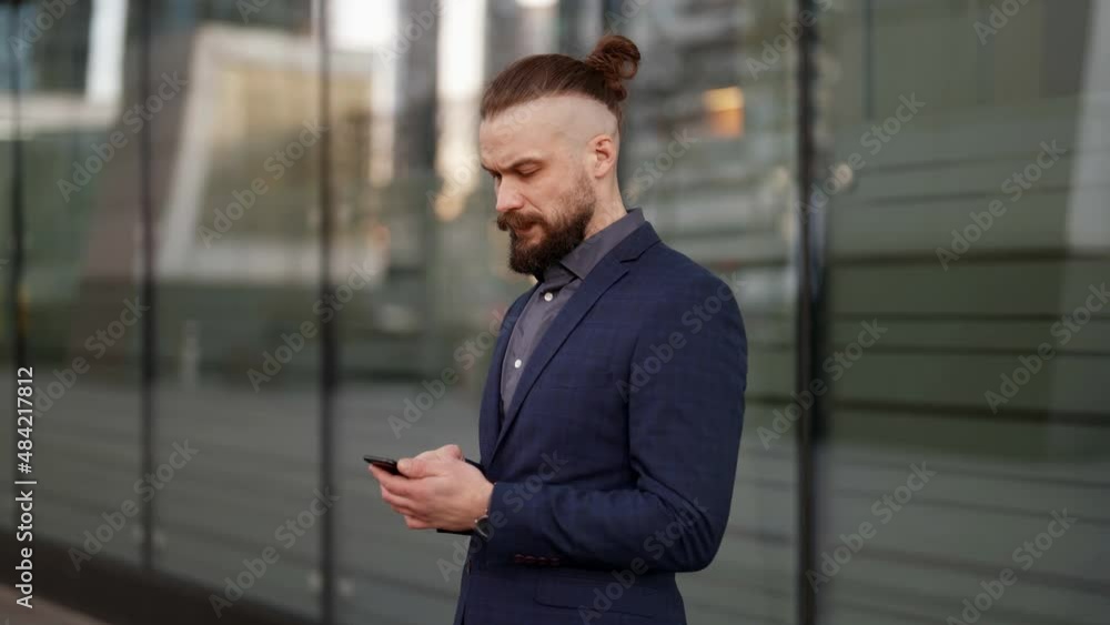 a mustachioed and bearded businessman in a plaid jacket is standing with a phone in hands and typing a text against a blurred glass wall. the camera is moving a mustachioed and bearded businessman in a plaid jacket is standing with a phone in hands and typing a text against a blurred glass wall. the camera is moving