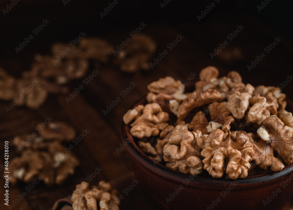 Walnut kernels close up in a brown ceramic bowl on a dark wooden background. Walnut kernels close up in a brown ceramic bowl on a dark wooden background.
