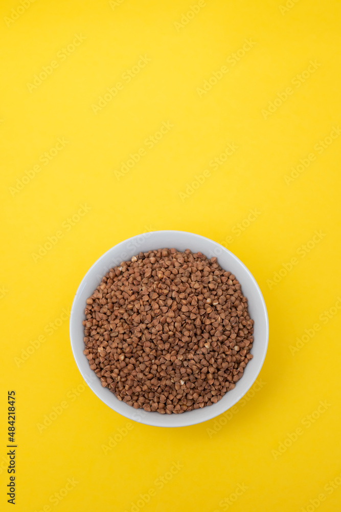 uncooked buckwheat in small white bowl on yellow uncooked buckwheat in small white bowl on yellow