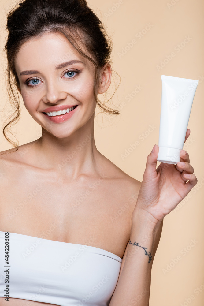 Cheerful model holding tube with lotion isolated on beige. Cheerful model holding tube with lotion isolated on beige.