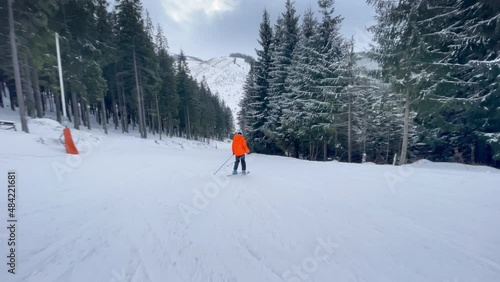 Action video of skier dressed yellow windproof ski clothes going downhill in the snowy spruces forest in Low Tatry Ski resort in Slovakia. Winter sports 4K concept.