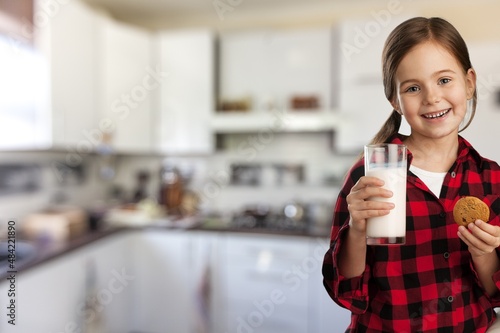 Portrait of sad girl holding glass of milk and dreaming, sitting on dinning table in kitchen interior