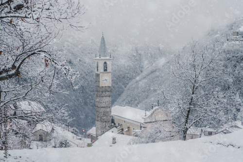 Winter snowfall over trees and old bell tower at Christmas, Sacco, Val Gerola, Valtellina, Sondrio province, Lombardy, Italy photo