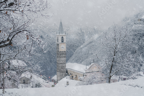 Winter snowfall over trees and old bell tower at Christmas, Sacco, Val Gerola, Valtellina, Sondrio province, Lombardy, Italy