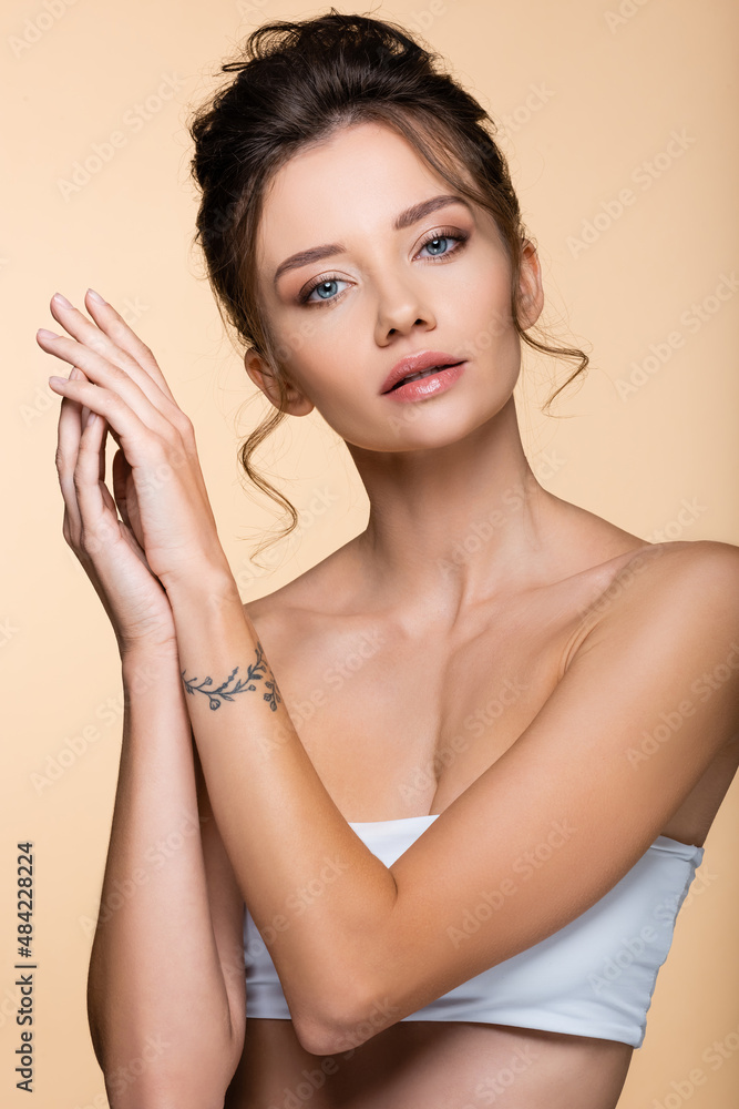 Young tattooed woman in top posing isolated on beige. Young tattooed woman in top posing isolated on beige.