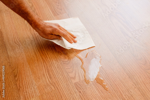 Man cleans a damp stain on the wooden floor of his house with absorbent kitchen paper.