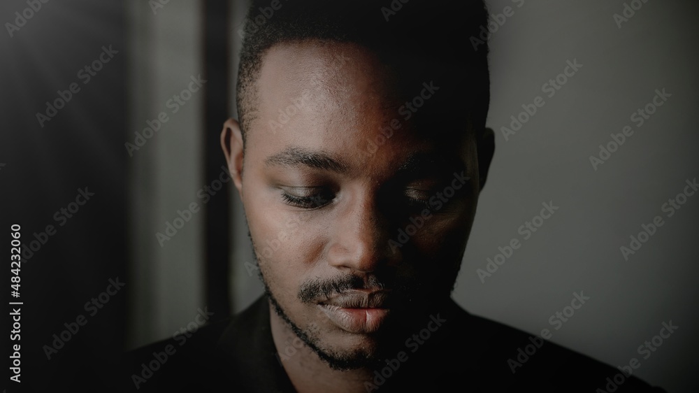 Depressed African man thinking about disappointed love and looking down in dark room.Concept of Broken Heart and Valentine's Day Depressed African man thinking about disappointed love and looking down in dark room.Concept of Broken Heart and Valentine's Day