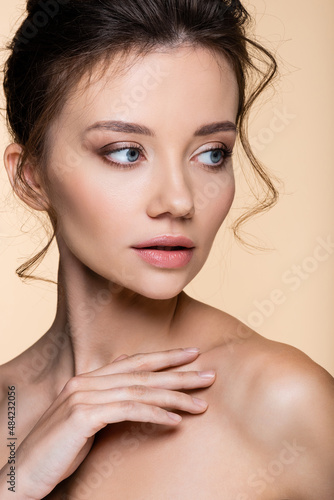 Portrait of pretty woman with naked shoulders looking away isolated on beige.