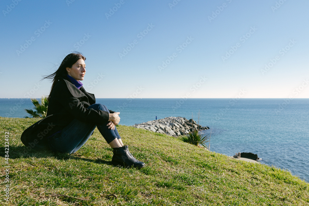 Middle-aged woman meditating in front of the sea on a winter day