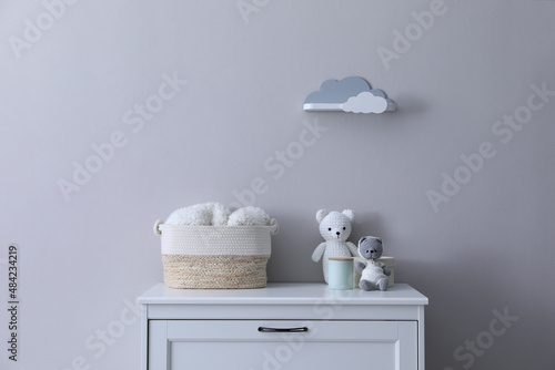 Child's toys, wicker basket and accessories on chest of drawers near light grey wall indoors © New Africa