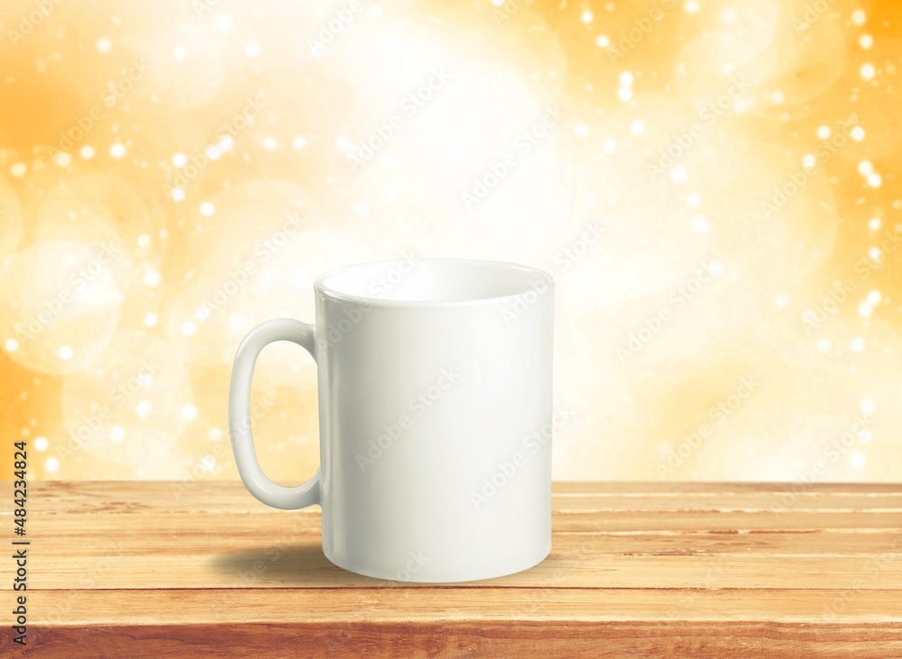 White mug on a wooden background with bright lights in the background. New Year and Christmas. White mug on a wooden background with bright lights in the background. New Year and Christmas.