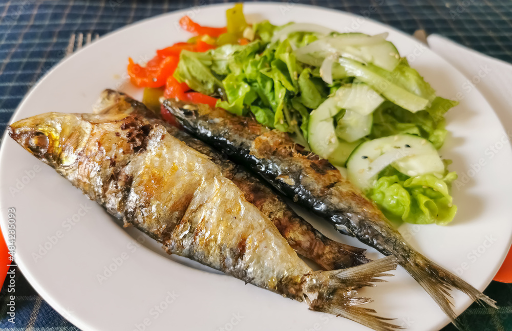 View of plated food, healthy fish meal, typical dish of Portuguese regional cuisine with grilled sardines with salad: red peppers, green peppers, sesame seeds, lettuce, onion and cucumber View of plated food, healthy fish meal, typical dish of Portuguese regional cuisine with grilled sardines with salad: red peppers, green peppers, sesame seeds, lettuce, onion and cucumber