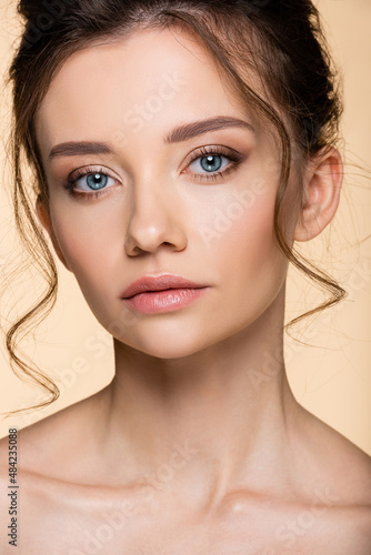 Portrait of young model with makeup looking at camera isolated on beige.