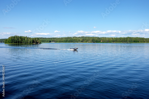 Beautiful view from the deck of the cruise ship going up the Lake Saimaa, Lappeenranta, Finland on a warm sunny day. A small motorboat glides gently on the lake.