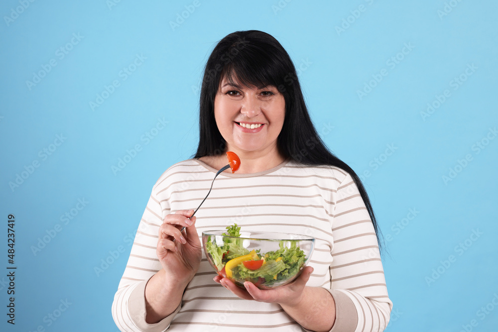 Beautiful overweight woman eating salad on light blue background. Healthy diet Beautiful overweight woman eating salad on light blue background. Healthy diet